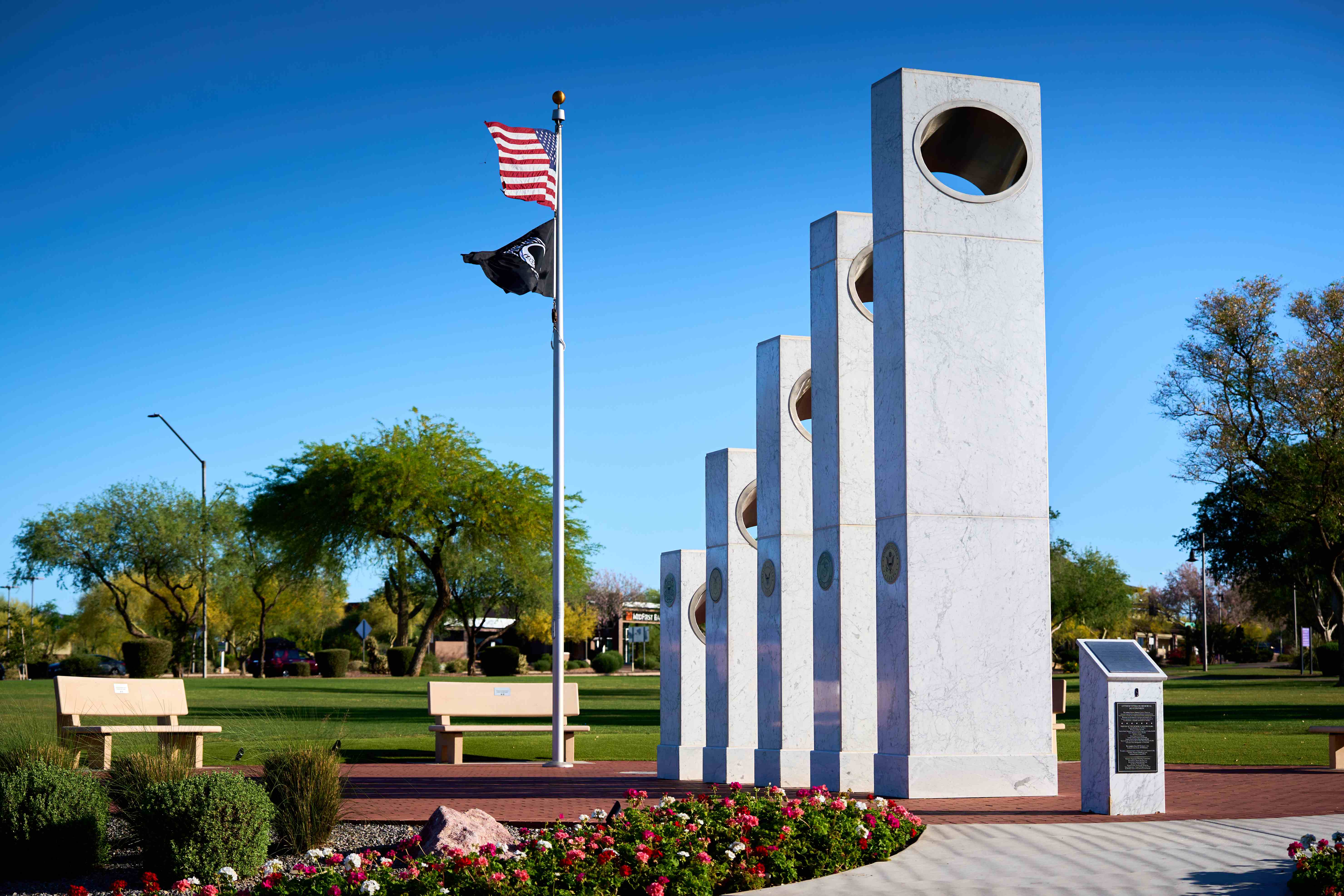 The Anthem Veterans Memorial in Anthem, Arizona — five ascending white marble pillars beside the U.S. and POW/MIA flags, with desert landscaping and mountain views